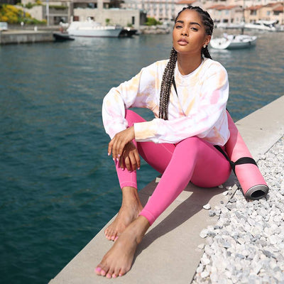 yogini sitting by the sea wearing pink leggings and tye dye sweater